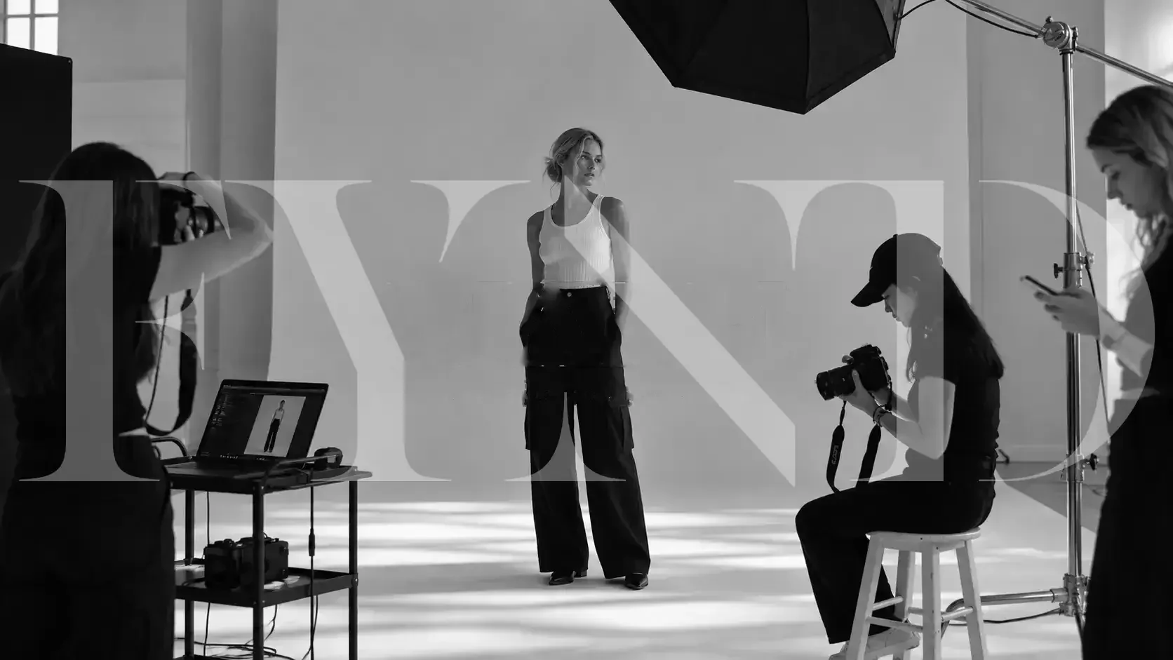 A model on a studio set with a photographer, a laptop and lights
